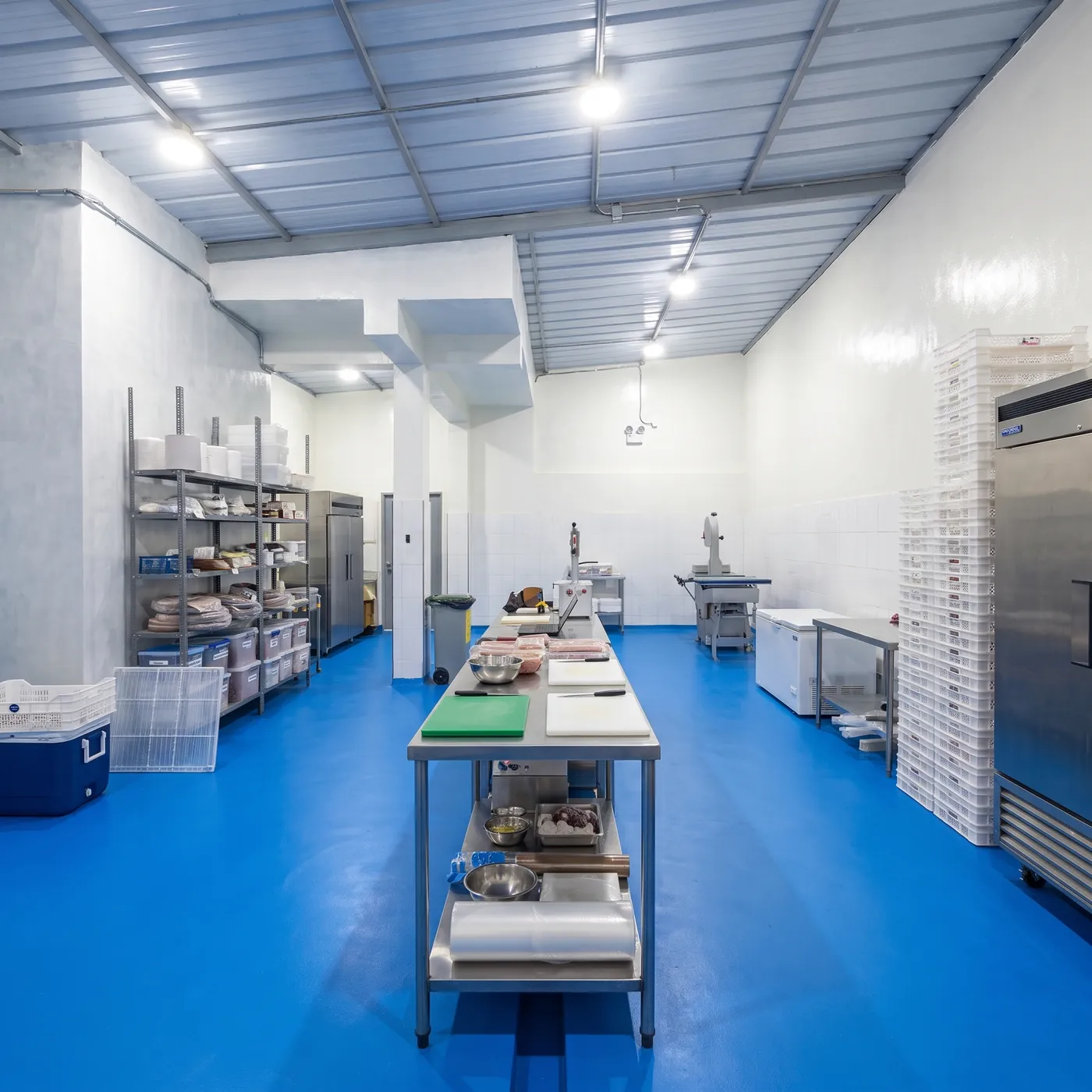 Cocina de producción de Realkan: mesa de acero inoxidable al centro, piso azul, paredes blancas y cámaras de frío.